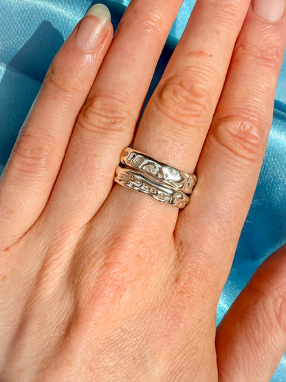 Hand wearing two silver rings against a blue background