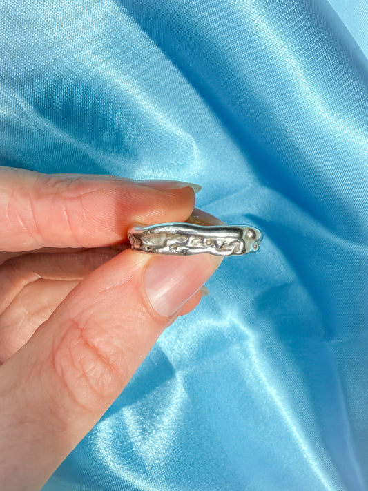 Silver molten ring held by a hand against a blue satin background