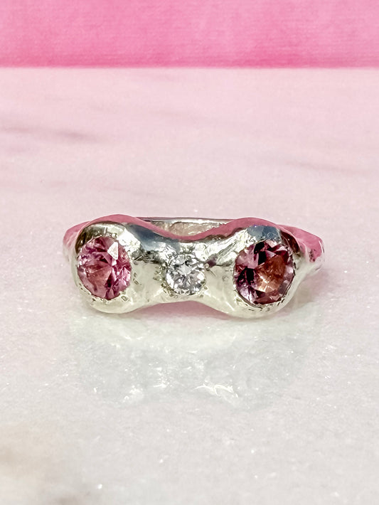 Silver ring with pink gemstones on a pink and white textured background