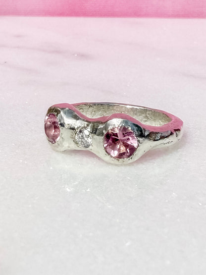 Silver ring with pink gemstones on a pink and white textured background other side view