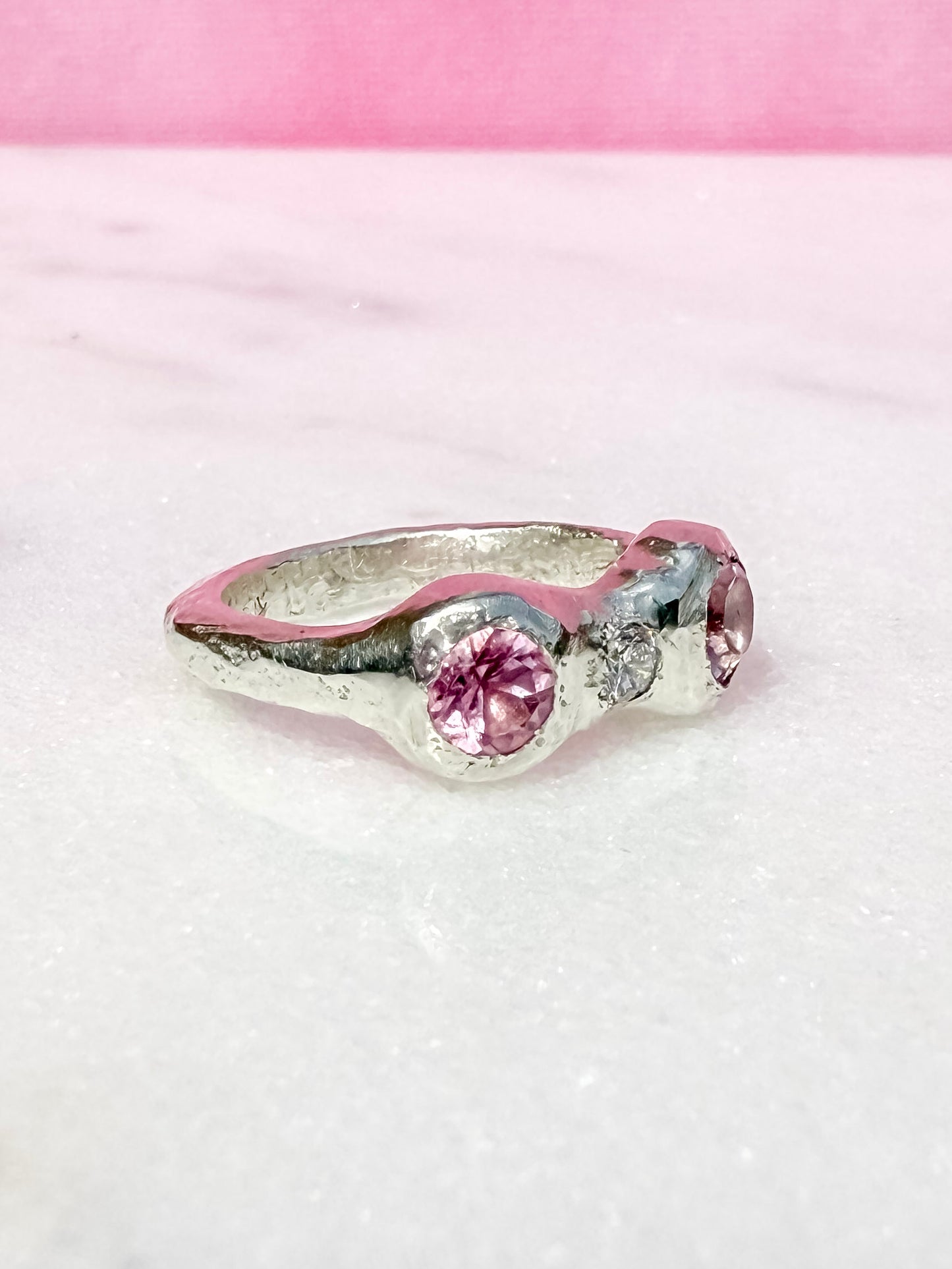 Silver ring with pink gemstones on a pink and white textured background side view