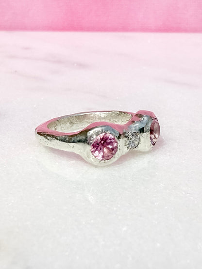 Silver ring with pink gemstones on a pink and white textured background side view