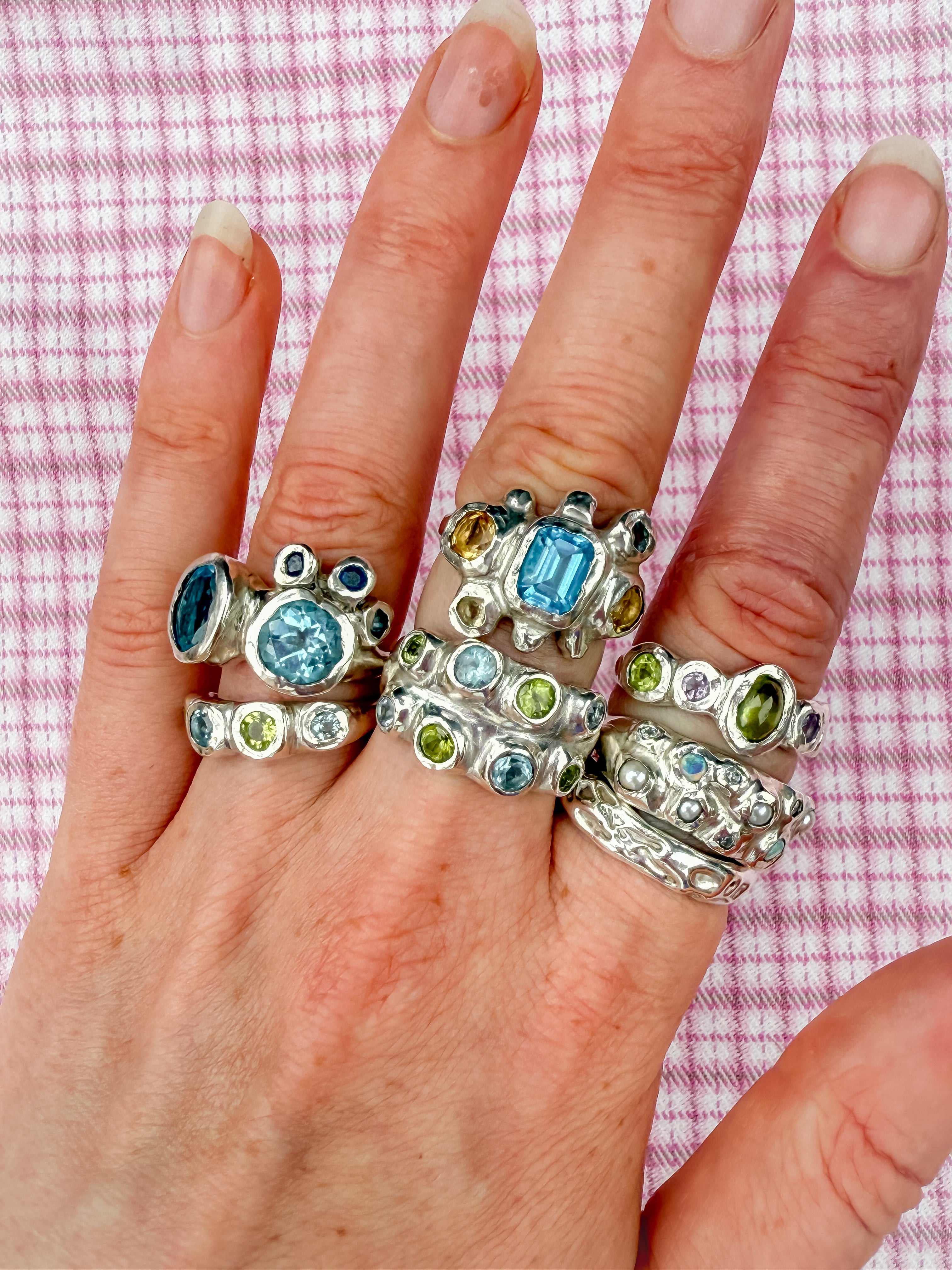 Dreamy silver rings with blue, green, yellow gemstones, opals and pearls on pink checkered background