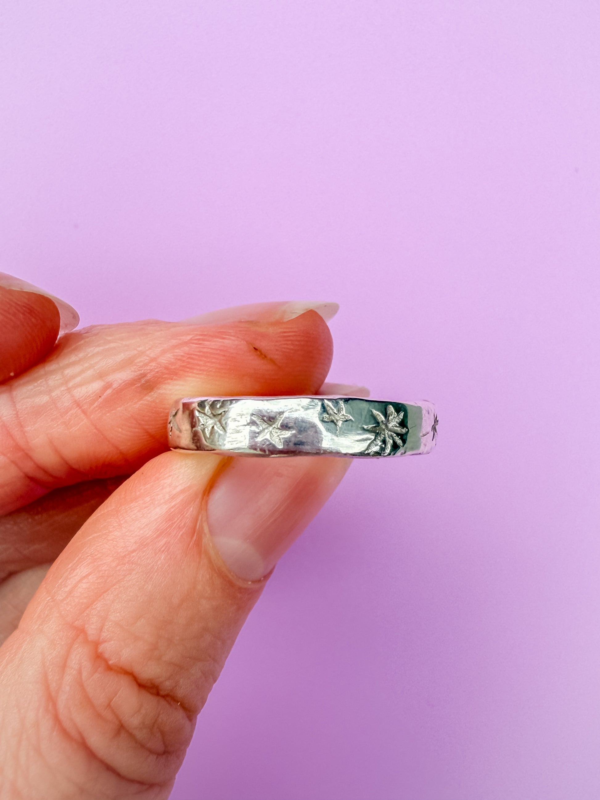 Silver ring with etched stars held between fingers against a purple background