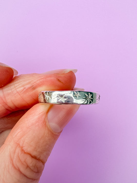 Silver ring with etched stars held between fingers against a purple background