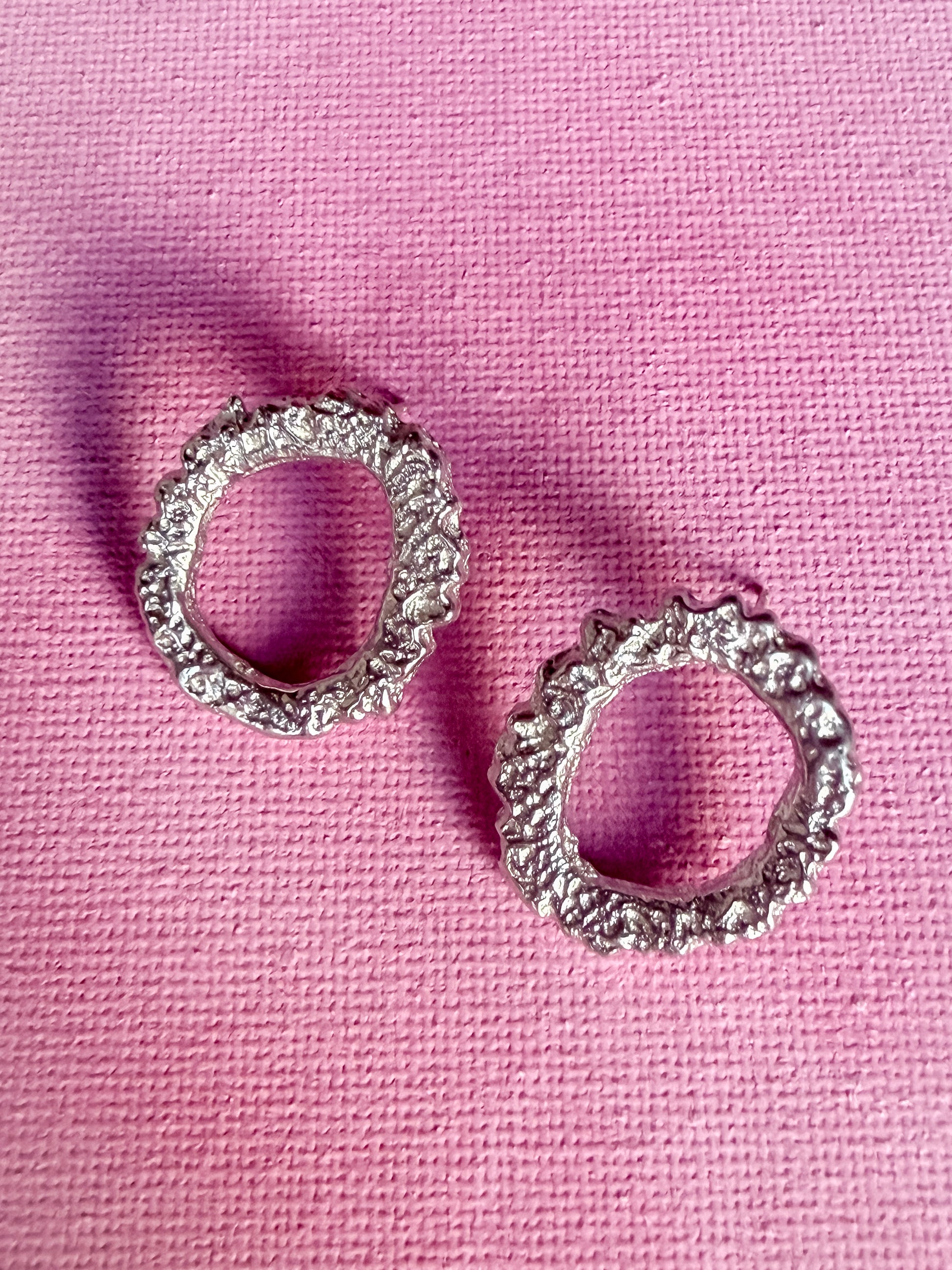 Textured circle silver stud earrings on pink background