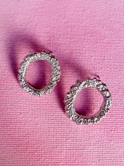 Textured circle silver stud earrings on pink background