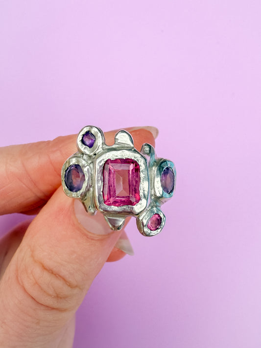 Silver bohemian ring with pink and purple gemstones held by a hand against a lilac background