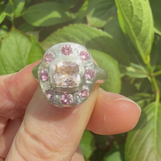 Cushion cut peach morganite pink tourmaline handmade silver ring against a leafy background sparkling in the sun
