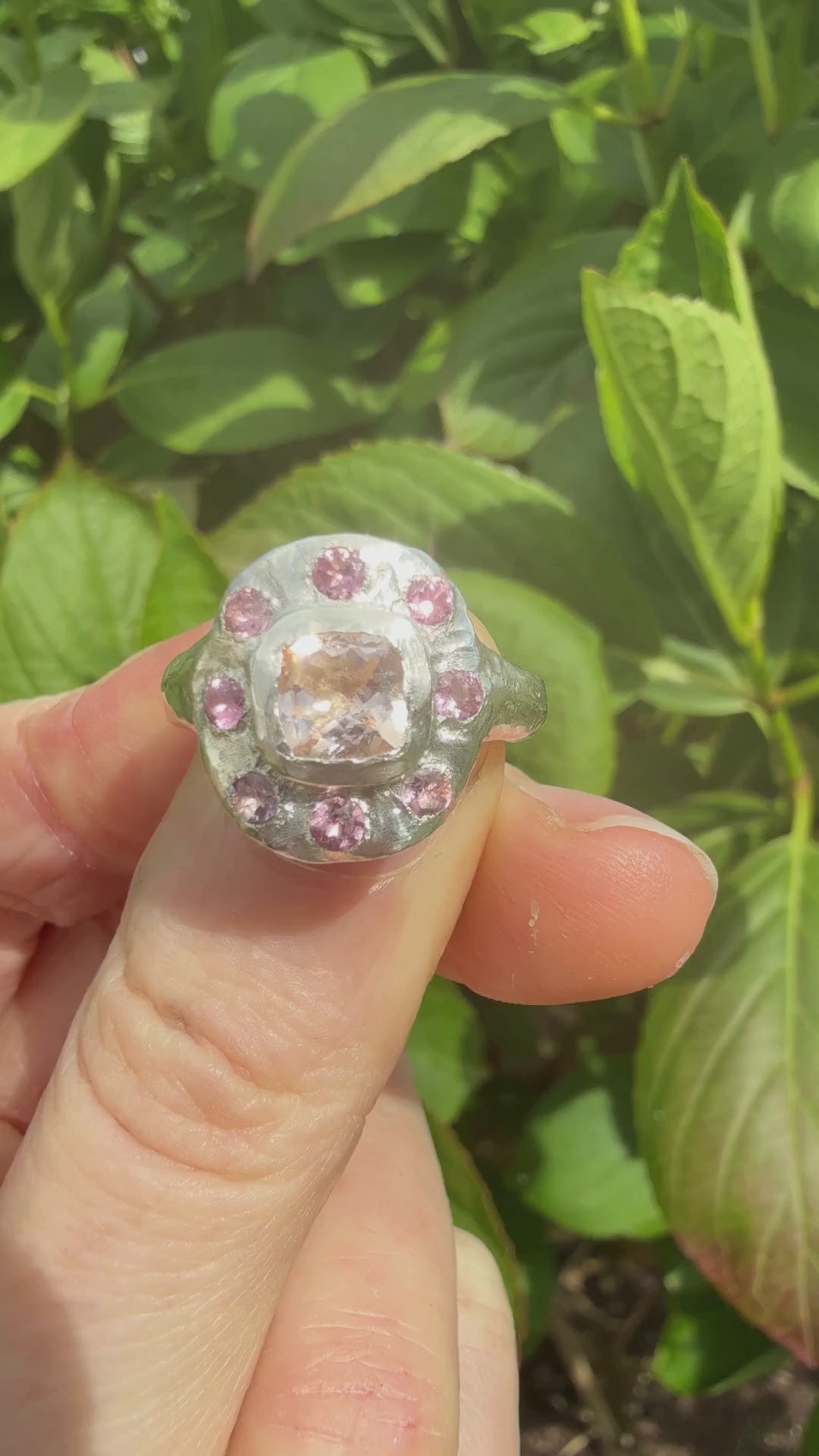 Cushion cut peach morganite pink tourmaline handmade silver ring against a leafy background sparkling in the sun