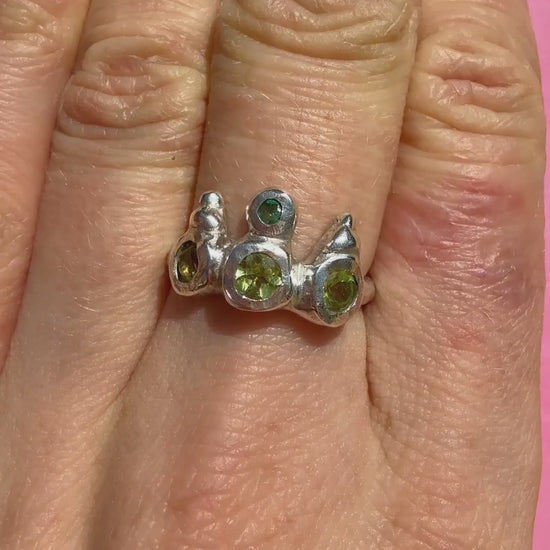 Peridot and emerald handmade silver ring on hand sparkling in sun against pink background