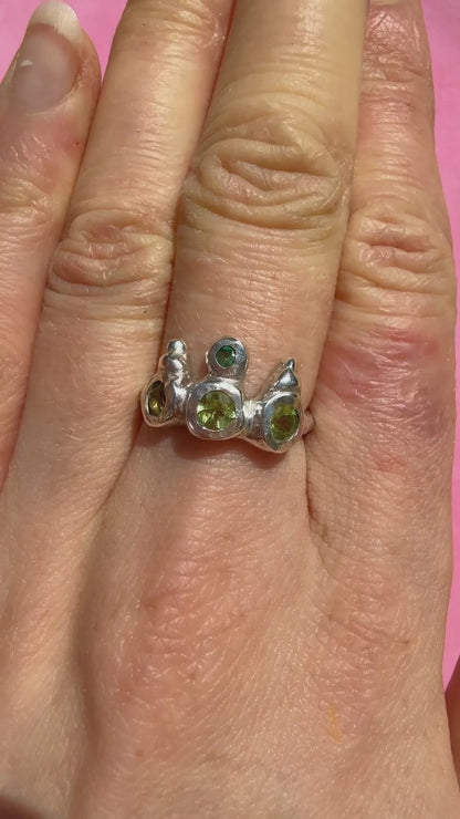 Peridot and emerald handmade silver ring on hand sparkling in sun against pink background
